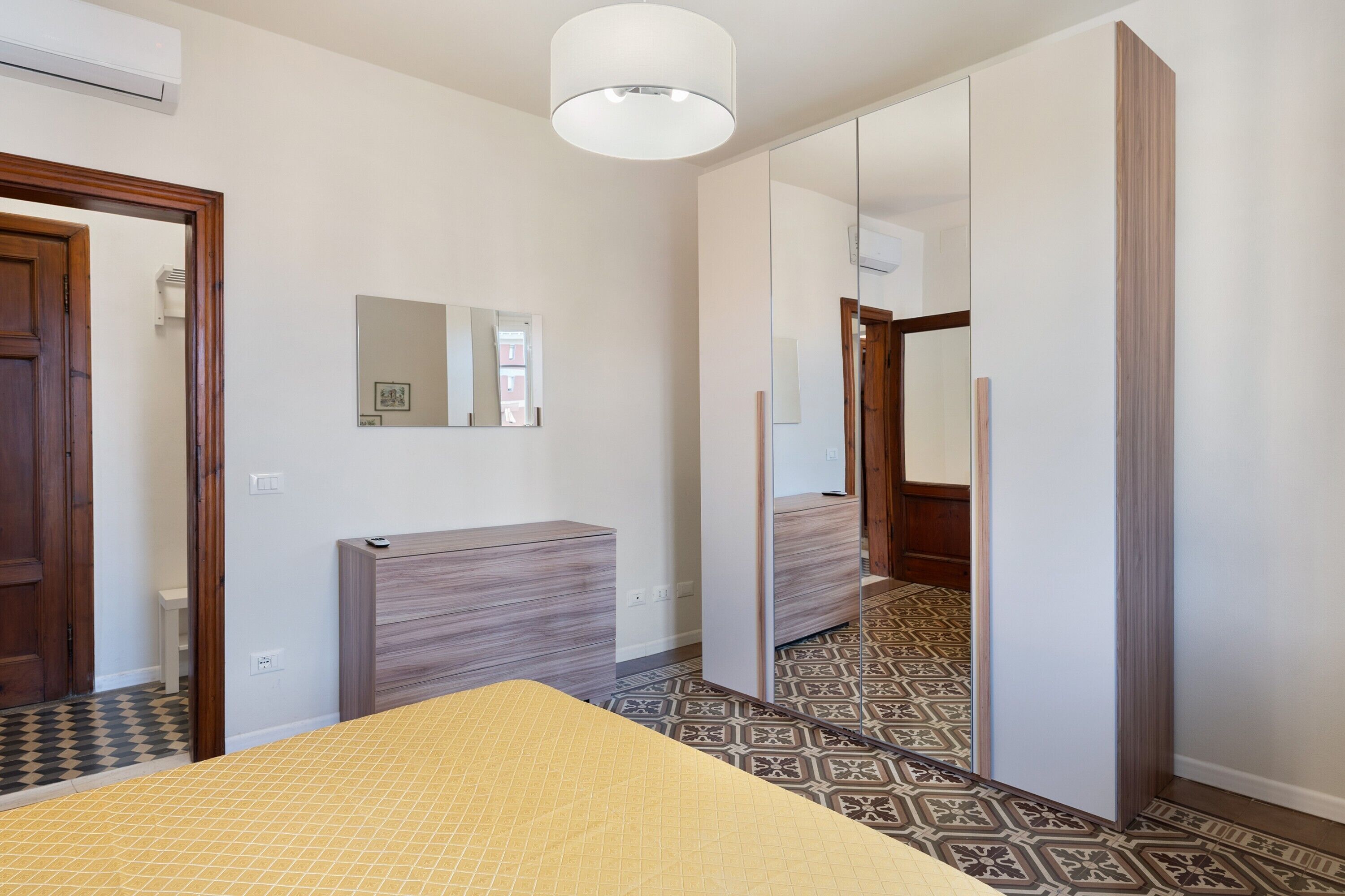 A hotel room with a bed, a bedside table, a mirror, and a wardrobe.