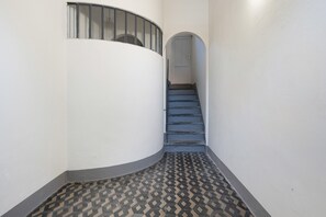 Ein schmaler Flur mit einer gewölbten Wand, einem gemusterten Boden und einer Treppe zu einer Tür.