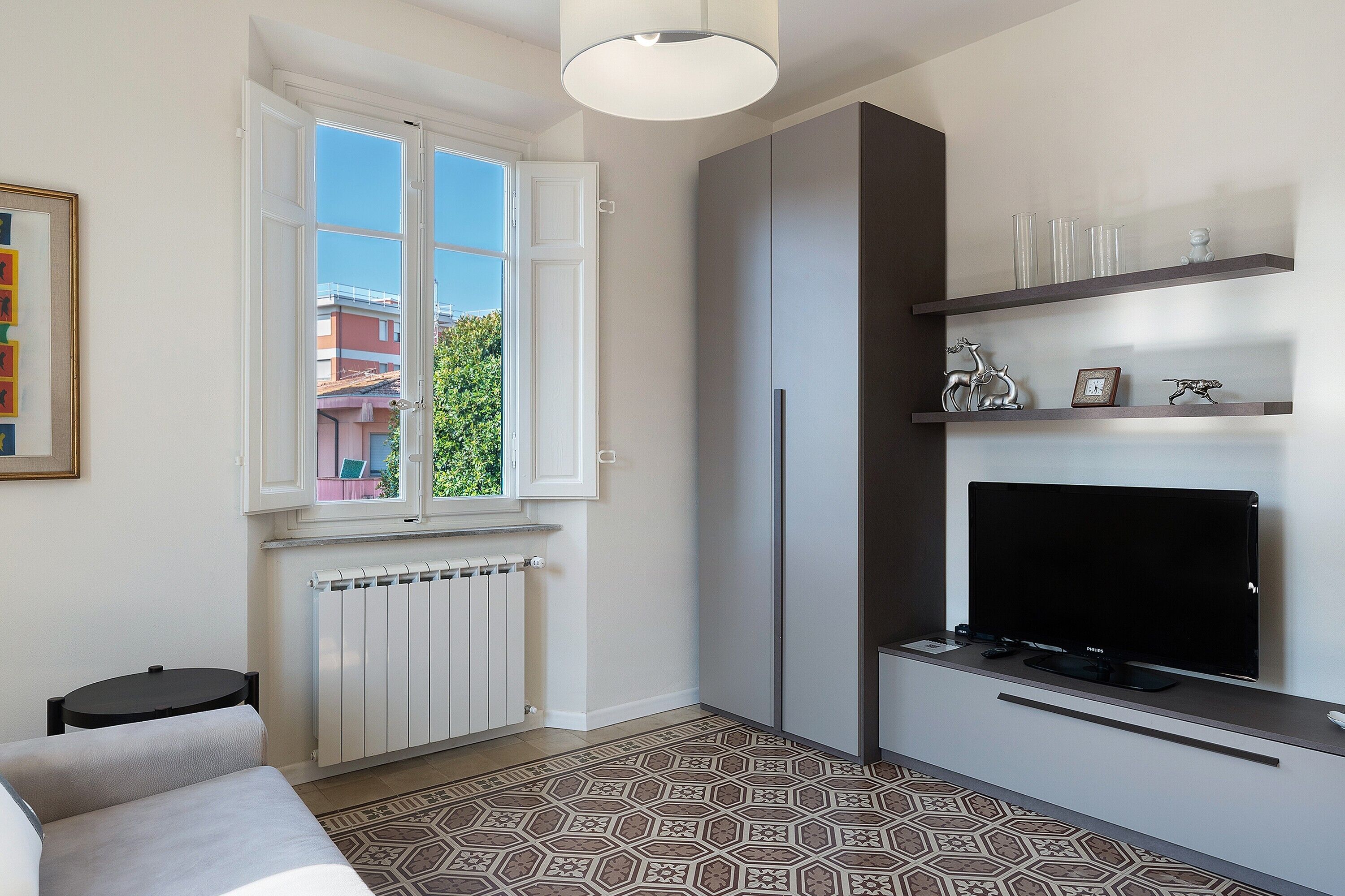 A compact living space with a television, shelving, and a window with an open door.