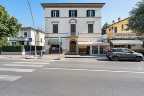 A street view with a building featuring a storefront labeled 'Pasticceria Belluomini' and a parked car.