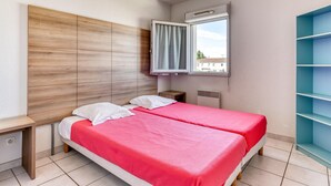 A bedroom with two beds, a window with a view, a built-in wardrobe, and a bedside table. - Spacious Coastal Stay for Six With AC (Le Grau-Du-Roi)