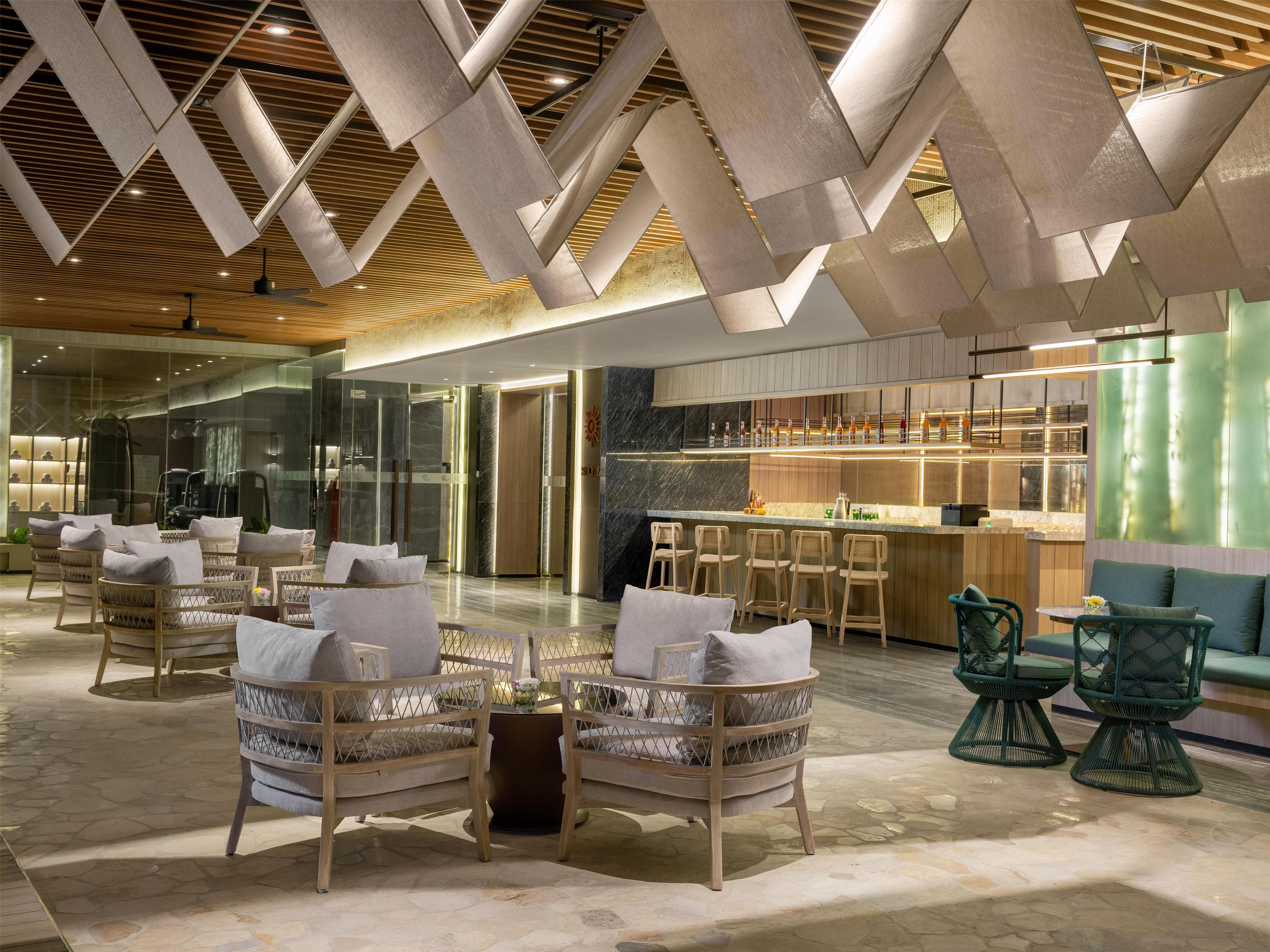 A modern hotel lobby with a bar area, seating arrangements, and a glass elevator.