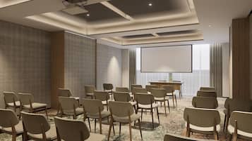 A conference room with rows of chairs, a projector screen, and a patterned wall.