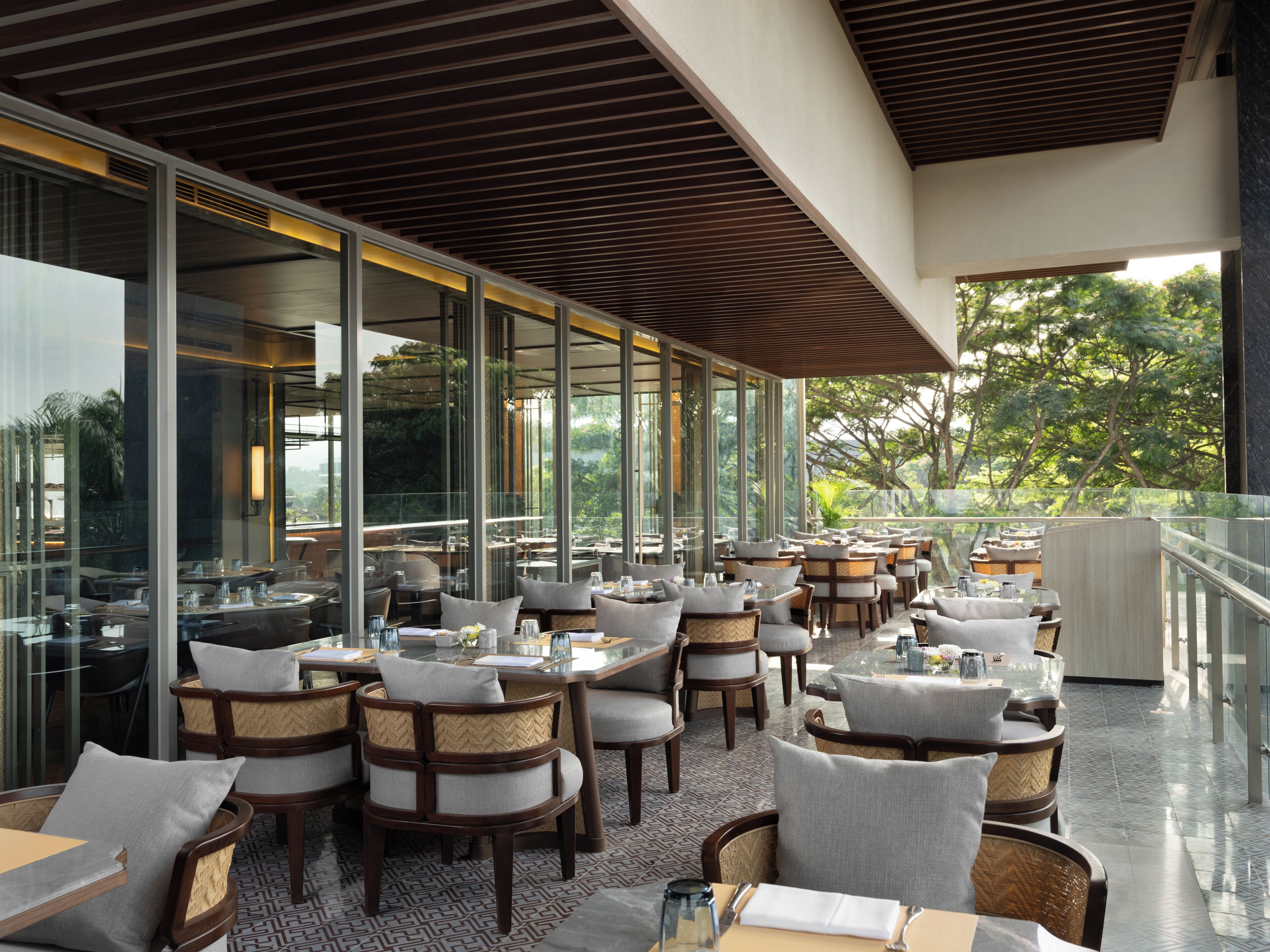 An outdoor dining area with tables and chairs, large windows, and a view of trees.