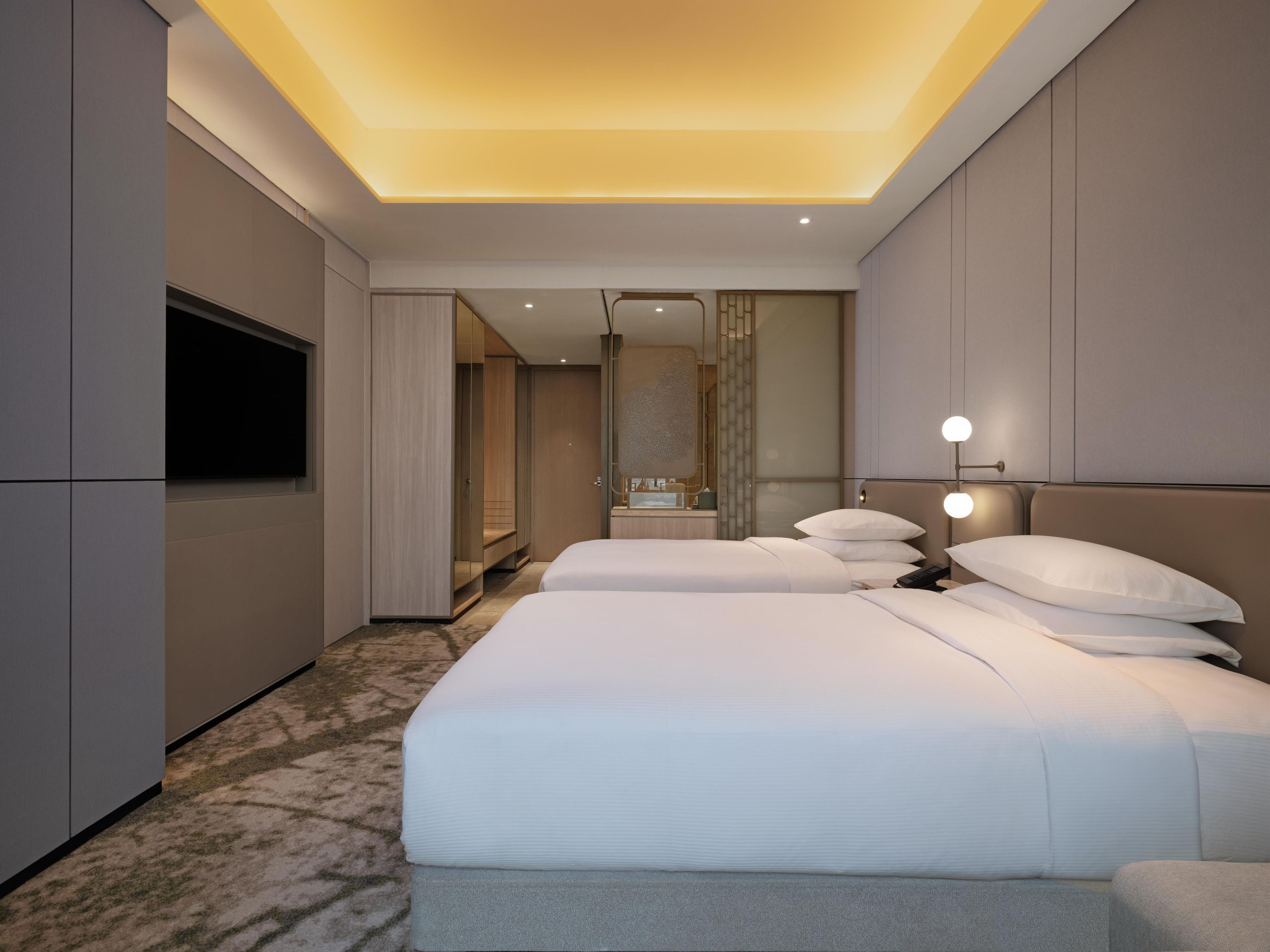 Una camera d'hotel moderna con un letto grande, lampade sui comodini, una TV e un armadio a muro.