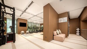 Een moderne sportschool met fitnessapparatuur, een televisie en een zithoek met een bord aan de muur.