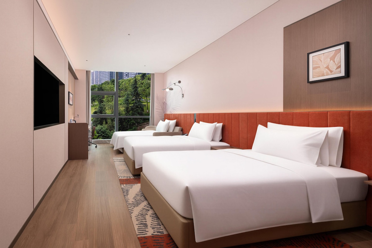A hotel room with two beds, a TV, a window with a city view, and a wall-mounted artwork.