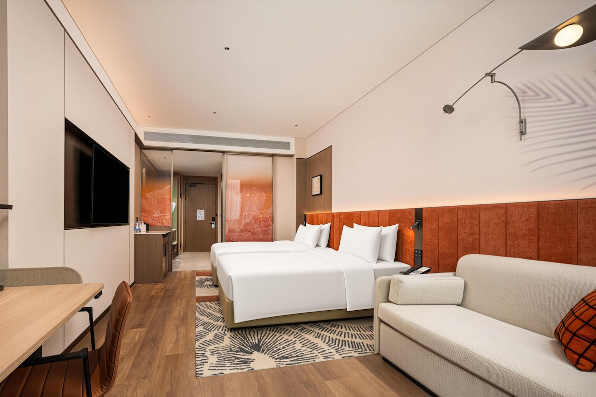 A modern hotel room with a bed, a sofa, a desk, and a television.