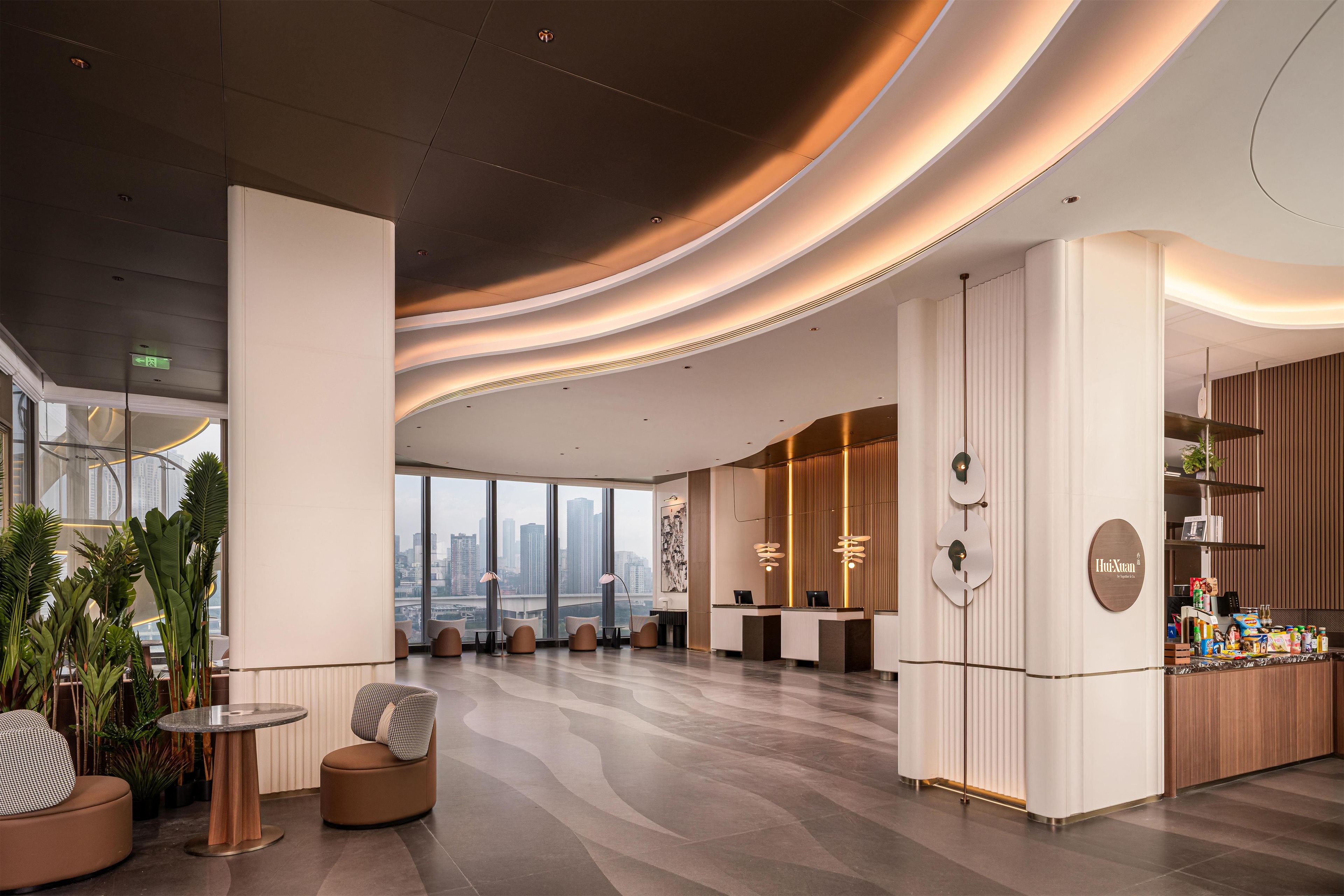 En modern hotellobby med en receptionsdisk, en sittgrupp och stora fönster med utsikt över staden.