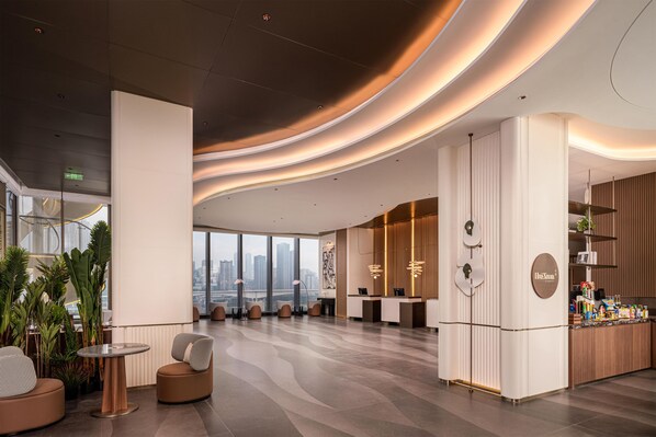 A modern hotel lobby with a reception desk, seating area, and large windows offering city views. - Hilton Garden Inn Chongqing Jiangbeizui (Chongqing)