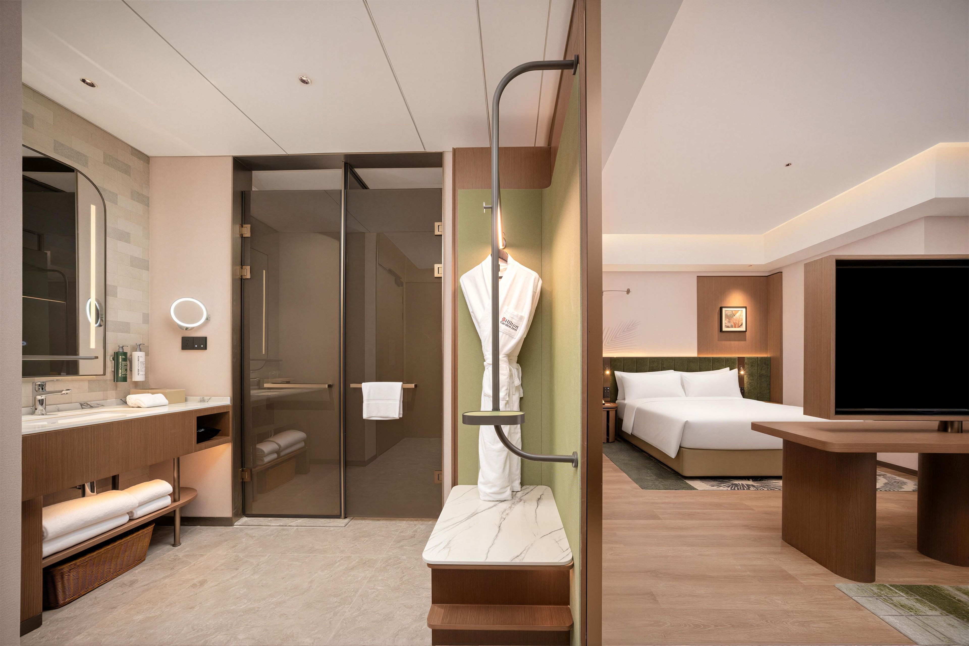 Habitación de hotel moderna con baño, una cama, un televisor y un perchero para bata.