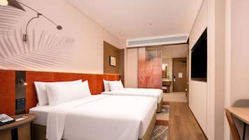A hotel room with two beds, a desk, a chair, a TV, and a bathroom visible through a glass partition.
