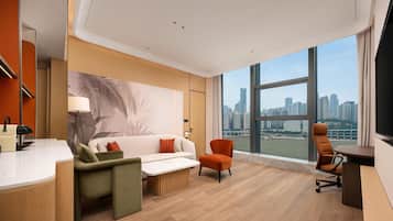 Habitación de hotel moderna con vista a la ciudad, un sofá, una silla, un escritorio y un ventanal grande.