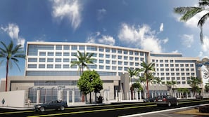 Un hotel moderno con una amplia fachada de vidrio, palmeras y un cielo despejado.