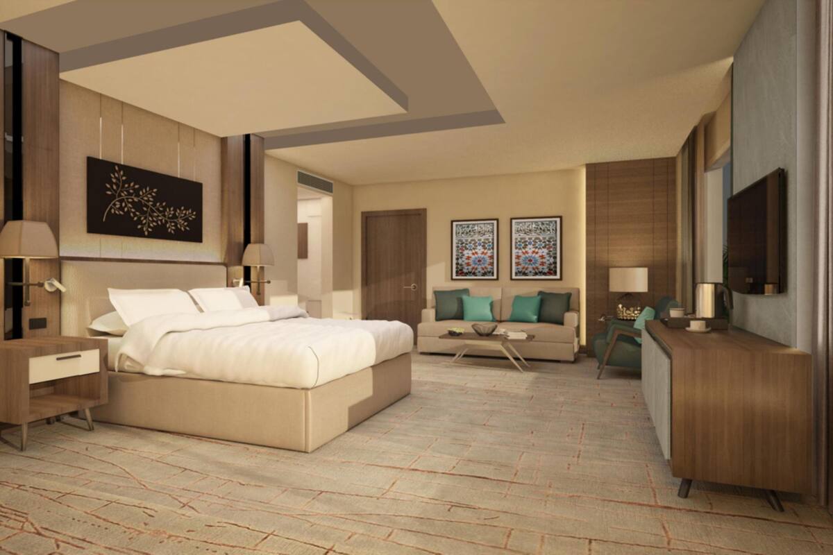 A modern hotel room with a large bed, a sofa, a coffee table, and a TV.