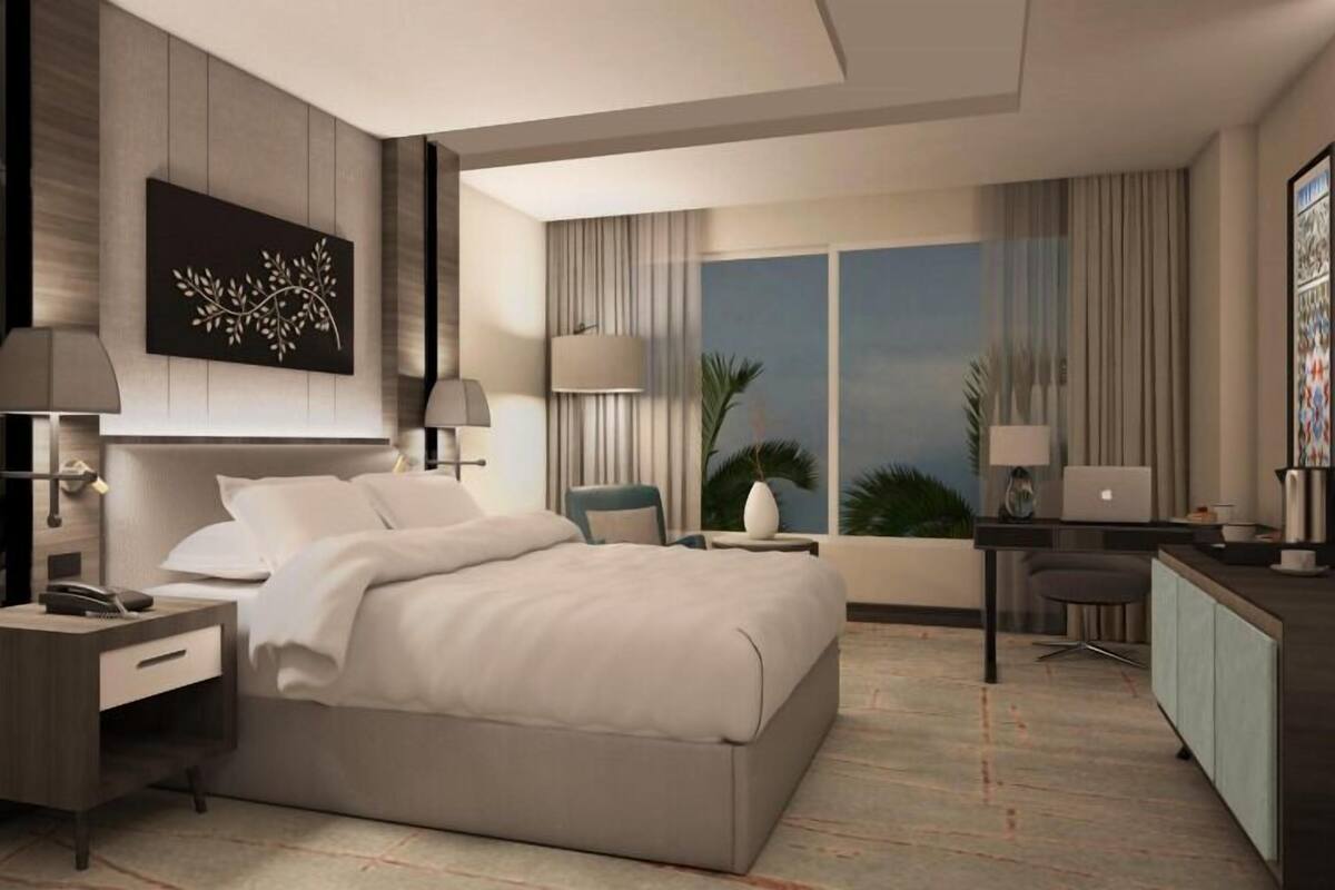 A modern hotel room with a large bed, bedside tables, a desk, and a view of the city.