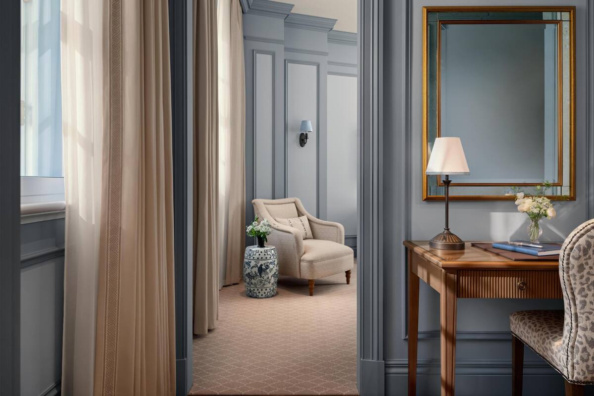 Habitación de hotel con un ventanal grande, una silla, una mesita con una lámpara y un espejo en la pared.