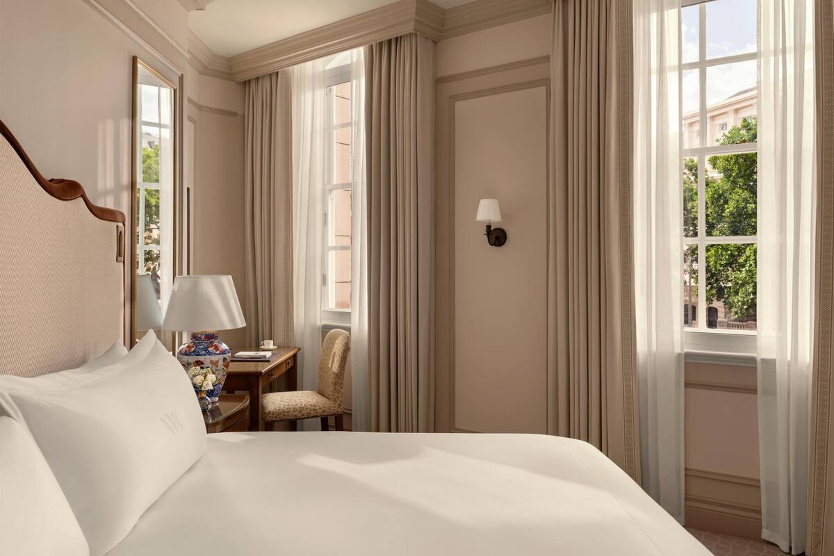 Habitación de hotel con una cama grande, un escritorio con lámpara, una silla y una ventana con cortinas.