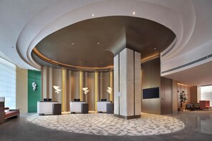 A modern reception area with a curved ceiling, multiple reception desks, and a patterned floor. - Hilton Garden Inn Shijiazhuang High-Tech Zone (Shijiazhuang)