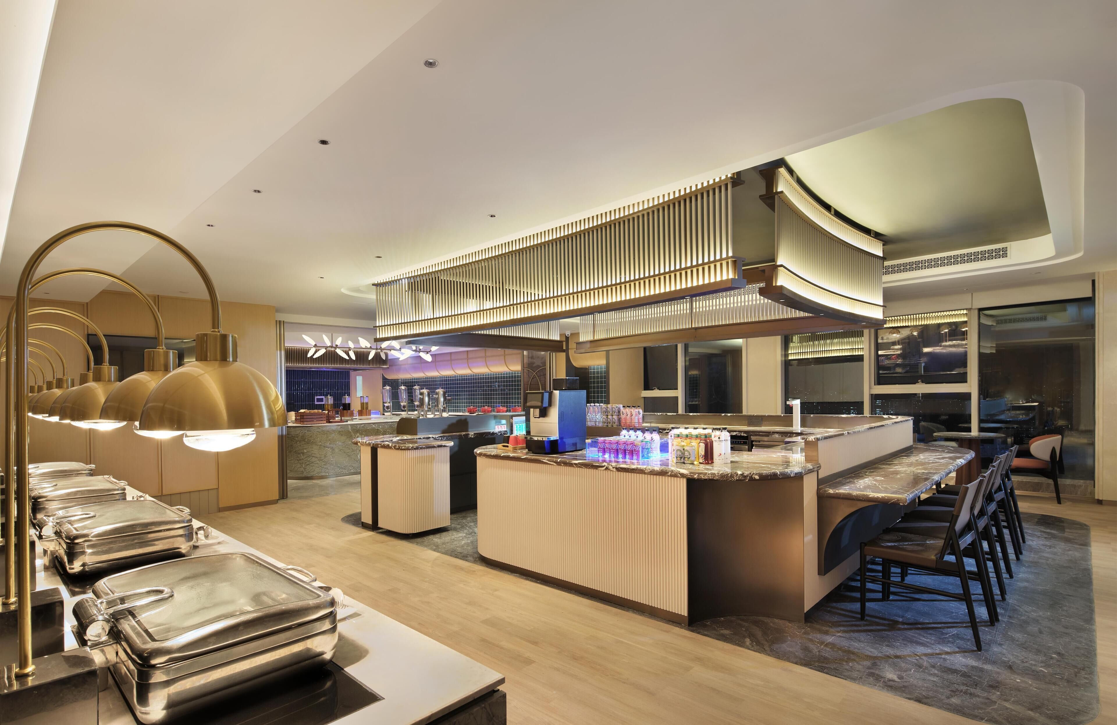 A modern hotel lobby with a central bar area, seating, and a decorative ceiling.