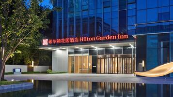 Un hotel Hilton Garden Inn con una fachada moderna, amplios ventanales y una piscina reflectante al frente.