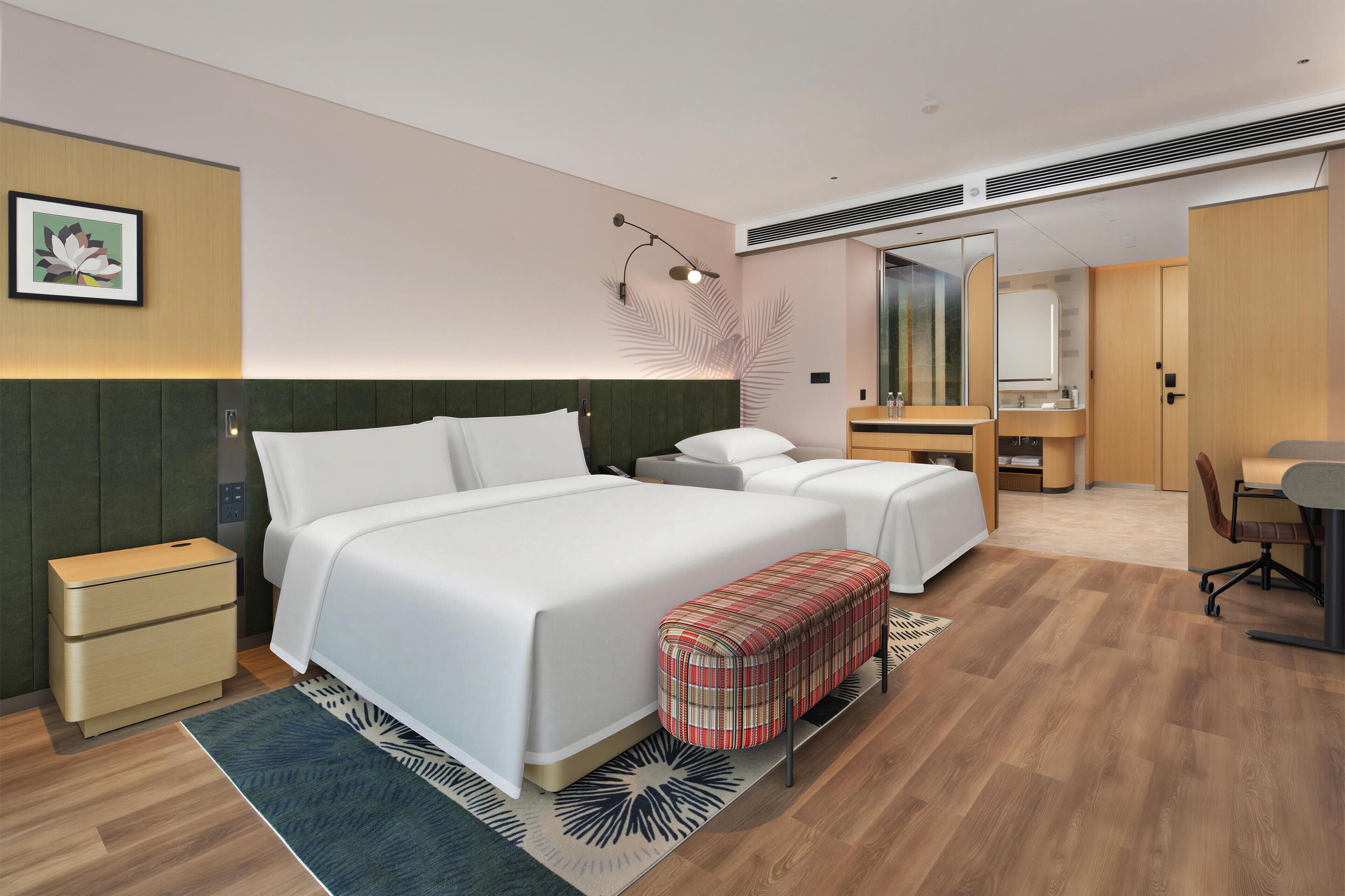A modern hotel room with a large bed, a desk, a chair, a small table, and a bathroom.