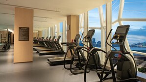 A gym with multiple treadmills, a clock, and a view of a cityscape through large windows. - Hilton Wenzhou (Wenzhou)