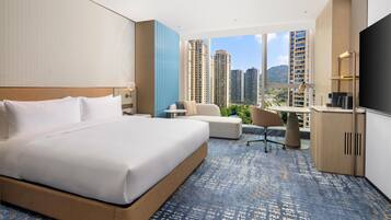 Habitación de hotel con una cama grande, un escritorio, una silla y vista a edificios altos.