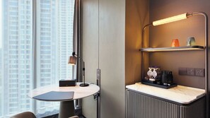 A modern hotel room with a round table, a desk with a lamp, a radiator, and a shelf with toiletries. - Hilton Wenzhou (Wenzhou)