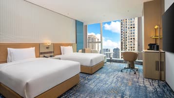 A hotel room with two beds, a desk, a chair, and a view of tall buildings.