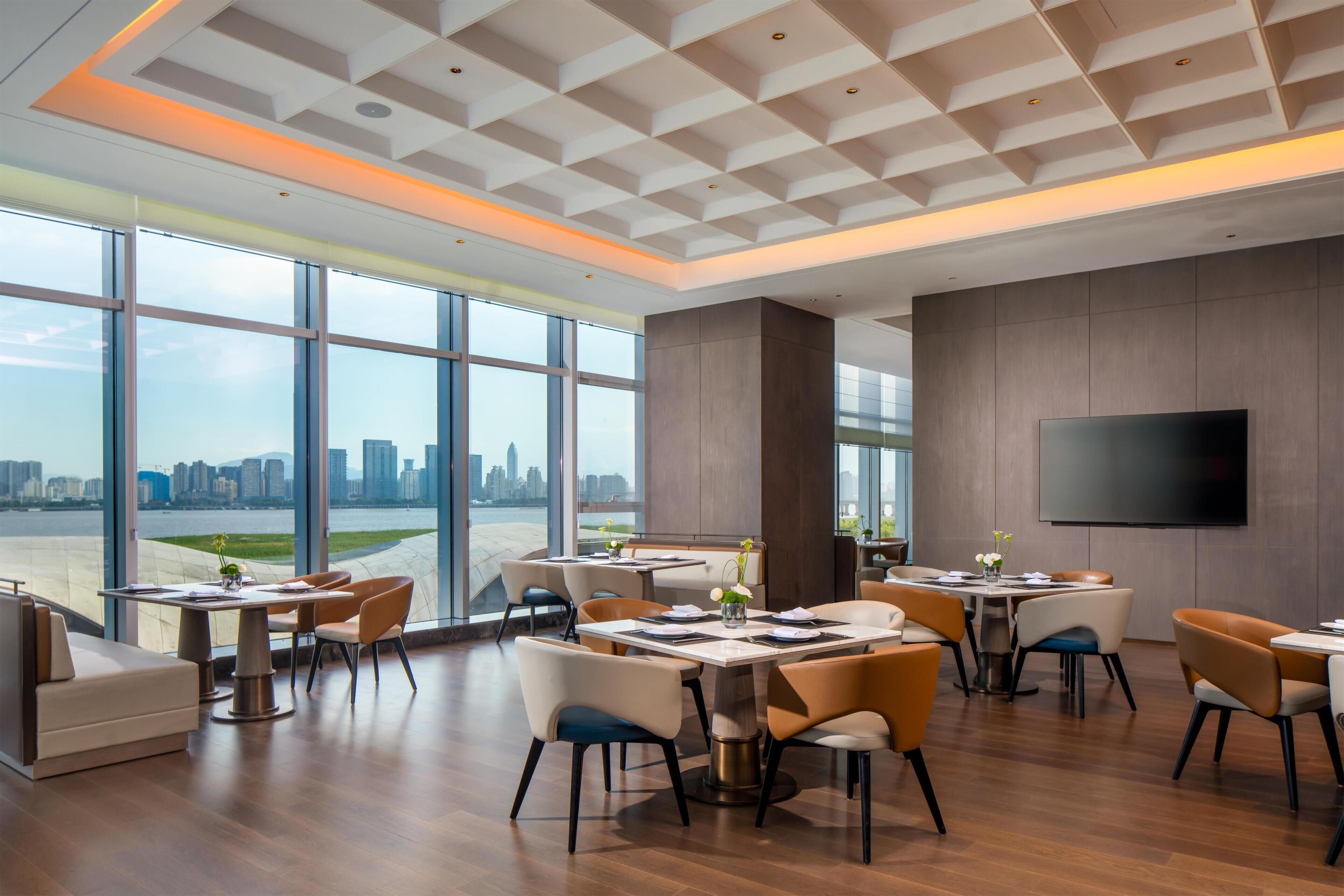 Un comedor moderno con ventanas amplias, un televisor de pantalla plana y vista al horizonte de la ciudad.
