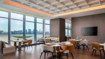 Un comedor moderno con ventanas amplias, un televisor de pantalla plana y vista al horizonte de la ciudad.