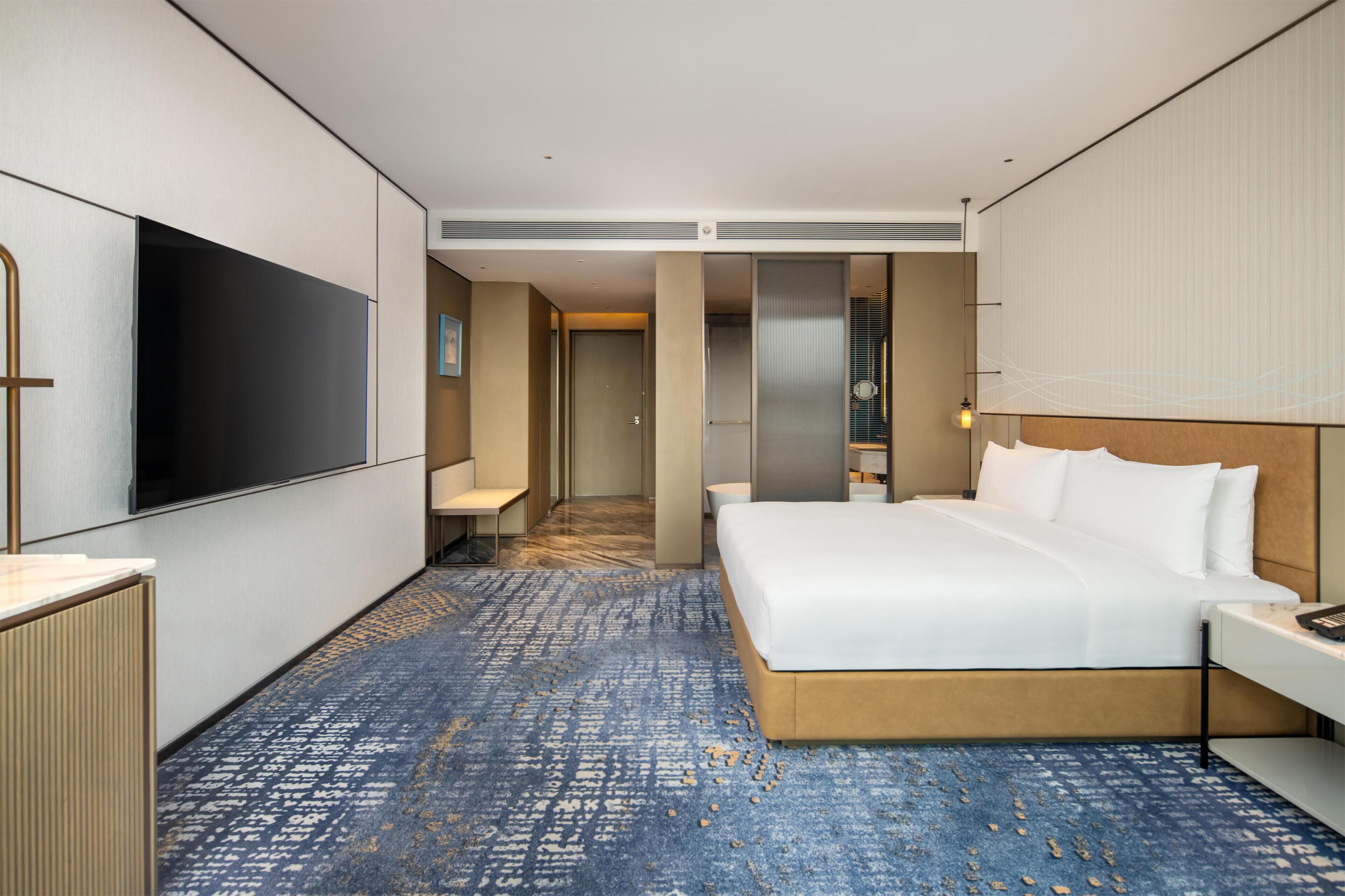 Habitación de hotel con una cama grande, televisor de pantalla plana, escritorio y vestidor.
