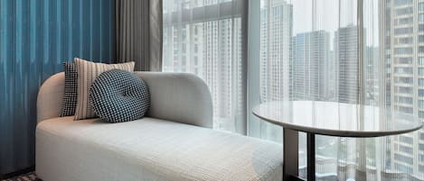 Una sala moderna con un sofá, almohadones estampados, una mesa redonda y vistas de rascacielos a través de cortinas traslúcidas.