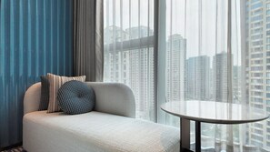 A modern living room with a sofa, patterned pillows, a round table, and a view of high-rise buildings through sheer curtains. - Hilton Wenzhou (Wenzhou)