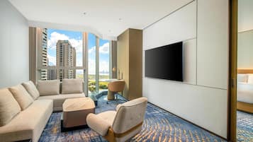 Habitación de hotel con un ventanal grande, un televisor de pantalla plana, un sofá, una silla y una pequeña mesa.