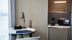 A hotel room with a round table, a chair, a lamp, a coffee machine, and a shelf with cups. - Hilton Wenzhou (Wenzhou)