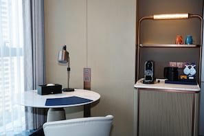 A hotel room with a round table, a chair, a lamp, a coffee machine, and a shelf with cups. - Hilton Wenzhou (Wenzhou)