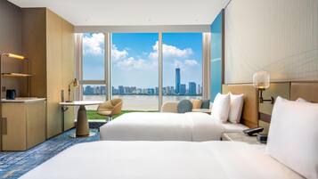 A hotel room with a large bed, a desk, a chair, and a view of a city skyline.