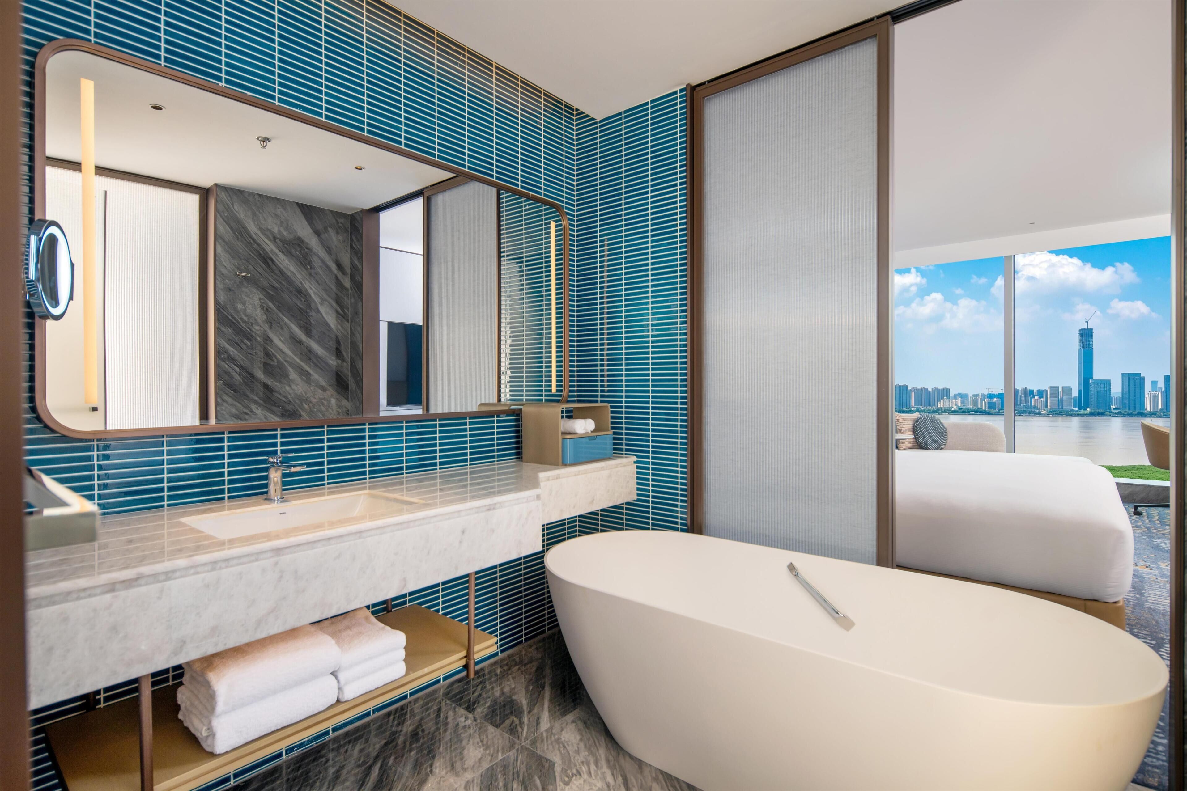 A modern bathroom with a large bathtub, a vanity with a mirror, and a view of a city skyline through large windows.