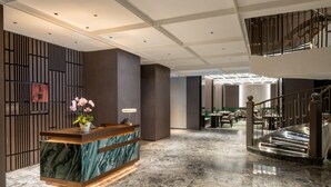 A hotel lobby with a reception desk, marble flooring, a staircase, and a seating area. - Hilton Wenzhou (Wenzhou)