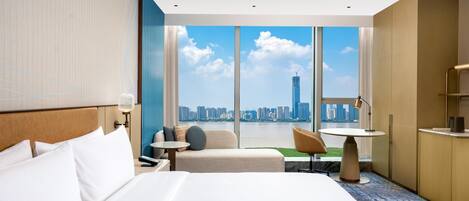A hotel room with a large bed, a seating area with a table, and a view of a city skyline.