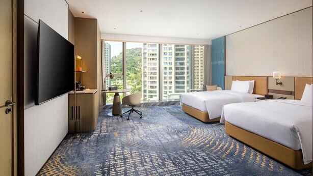 A hotel room with two beds, a desk, a TV, and a view of high-rise buildings. - Hilton Wenzhou (Wenzhou)