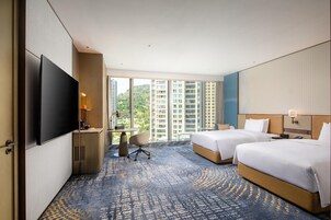 Quarto de hotel com duas camas, uma escrivaninha, televisão e vista para edifícios altos.