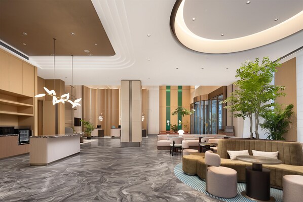 A modern hotel lobby with a reception desk, seating area, and a large window.