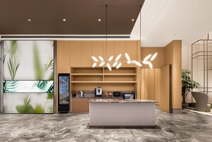 En modern entréhall med ett marmorgolv, en central ö med en kaffemaskin och en stor vägg med ett bladmotiv.