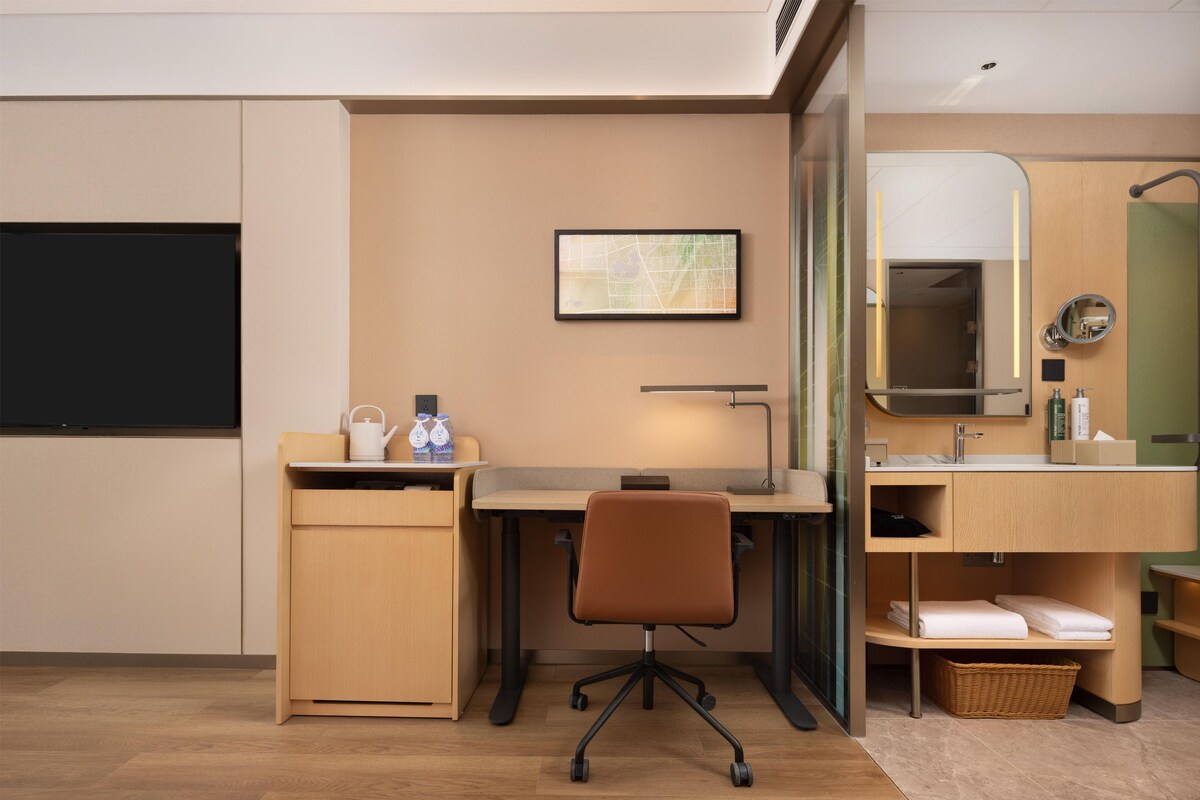 A hotel room with a desk, chair, and a small kitchenette area.