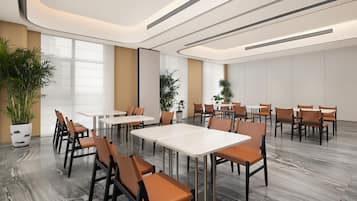 A modern conference room with white tables and brown chairs, large windows, and potted plants.