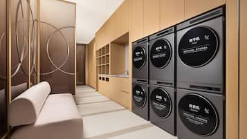 Un moderno cuarto de lavado con lavadoras y secadoras empotradas, una zona de estar con sofá y un elemento decorativo circular en la pared.