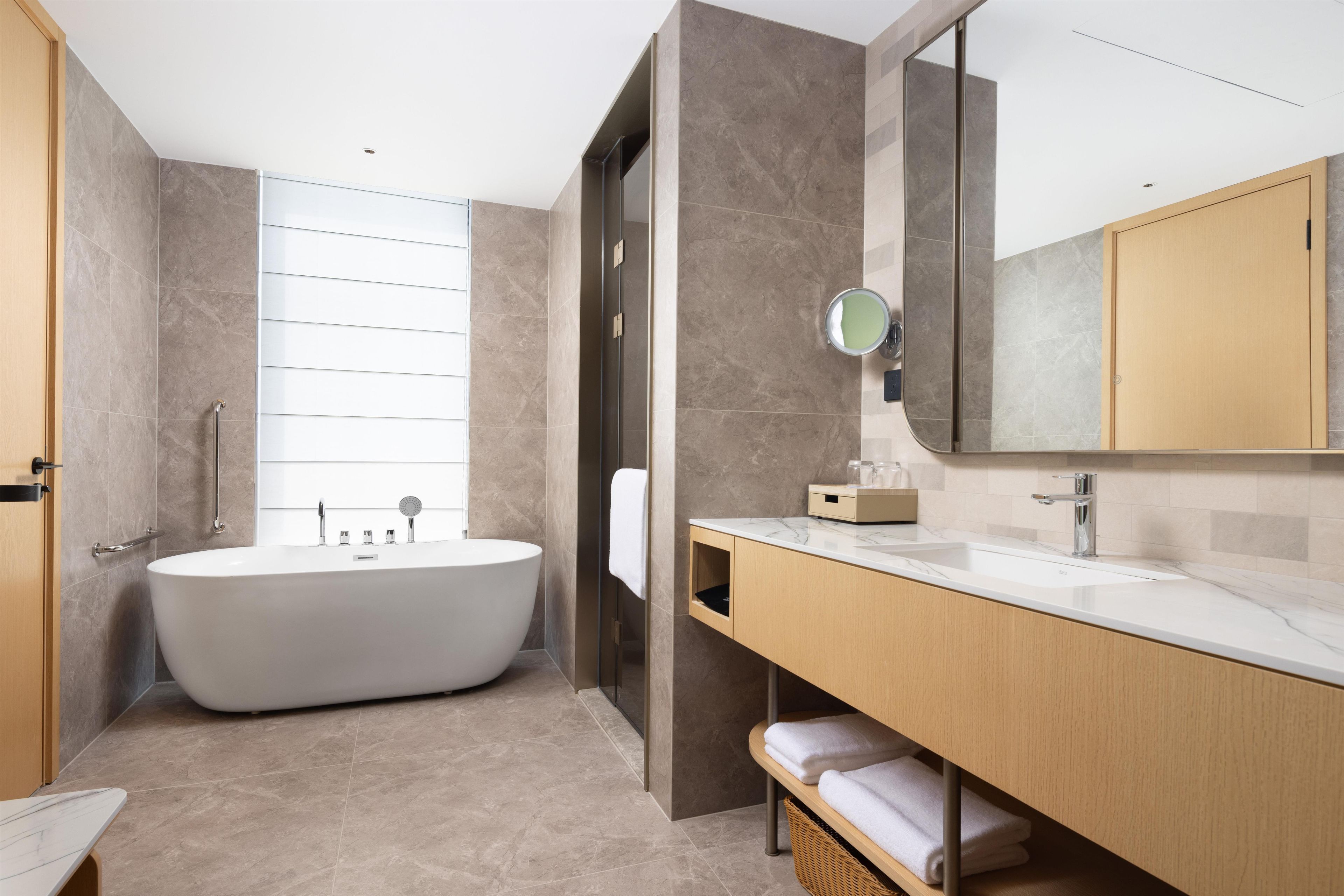 Ein modernes Badezimmer mit einer freistehenden Badewanne, einem großen Spiegel und einem Holzwaschtisch.